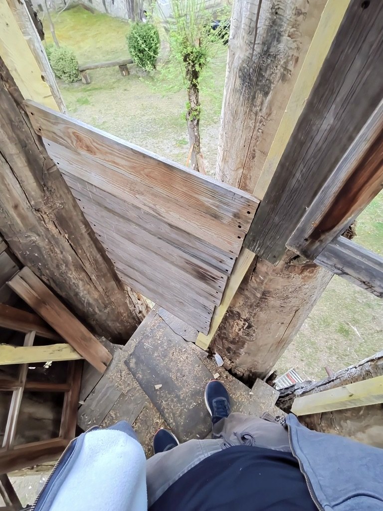 View down between timber levels past a boarded panel to a lower deck and the trunk