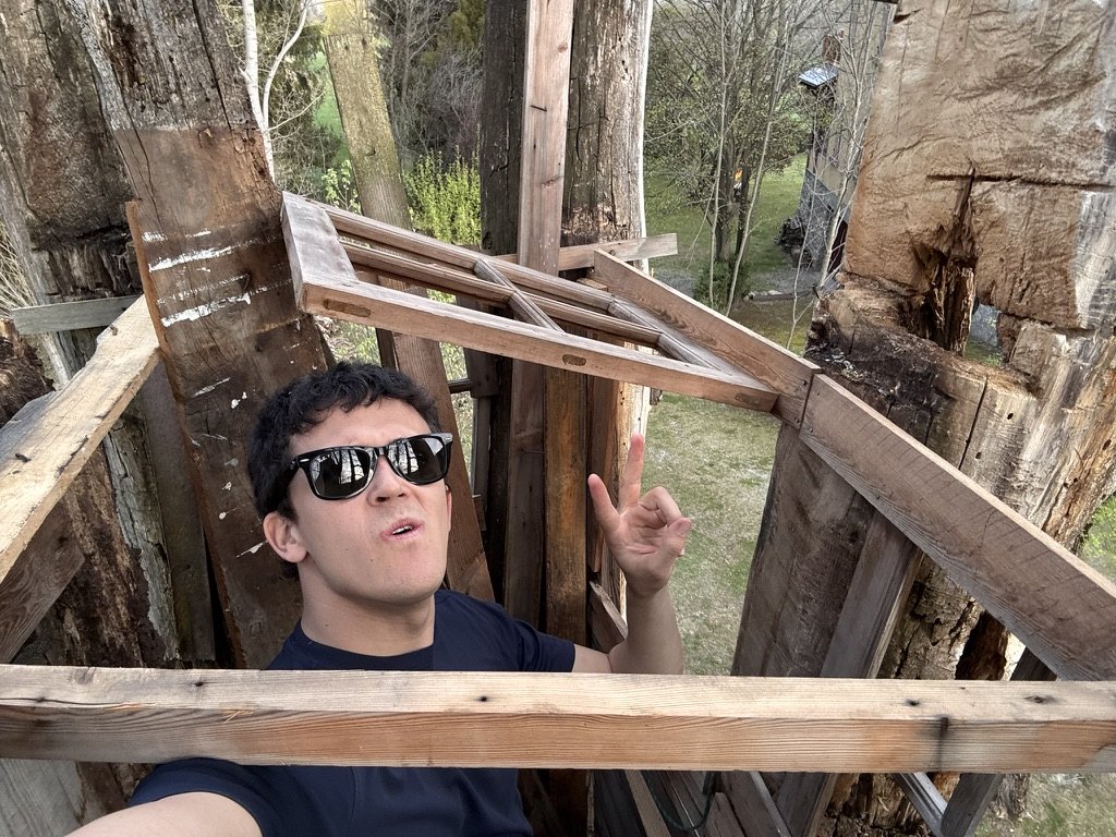 Raimon in sunglasses inside the timber structure, pointing at a wooden window frame