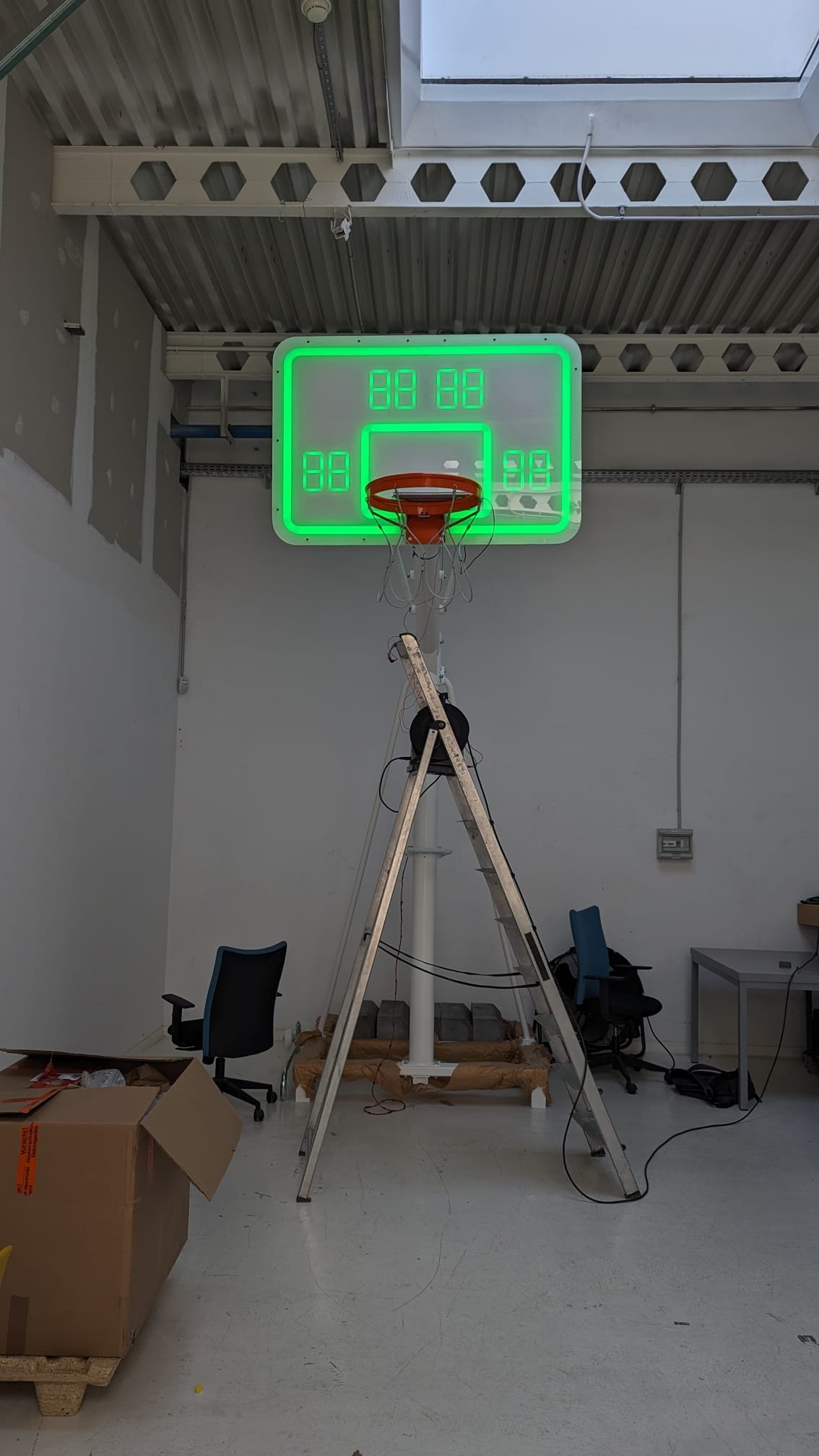 Smart basketball hoop prototype with green LED border and seven-segment scoreboard in a workshop