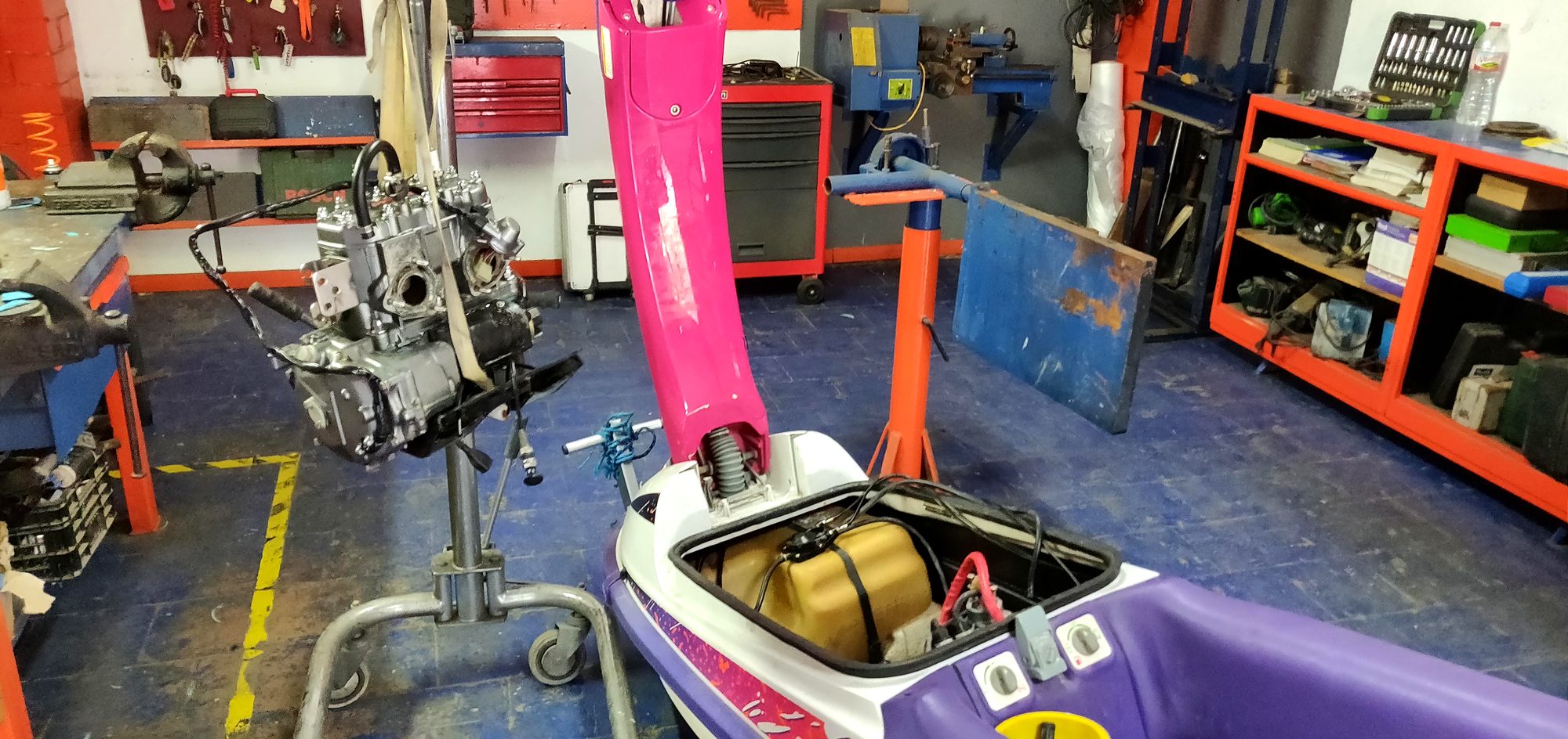 Silver twin-cylinder engine hanging from a hoist beside the jet ski hull