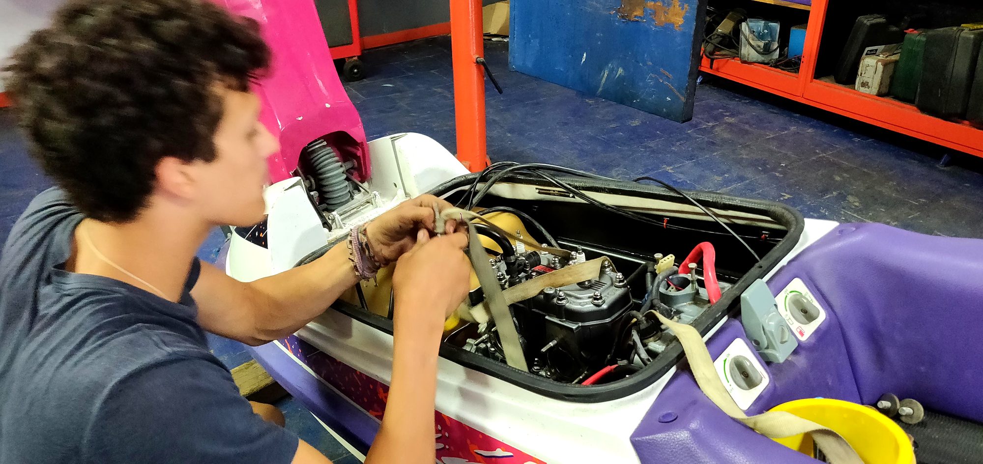 Person leaning over the open engine bay with a canvas strap around the engine