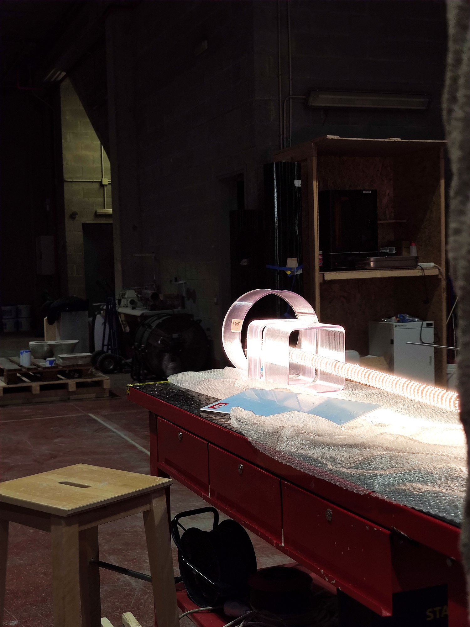 Glowing LED strip threaded through clear acrylic diffuser forms on a red workshop bench