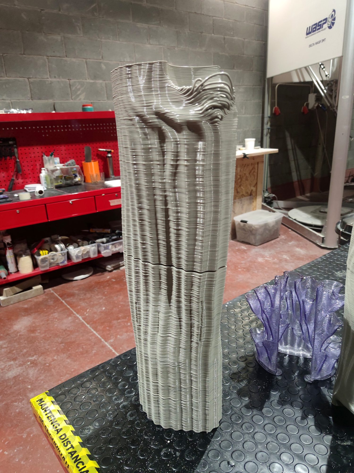 Grey layered 3D-printed pillar prototype next to a WASP 3D printer