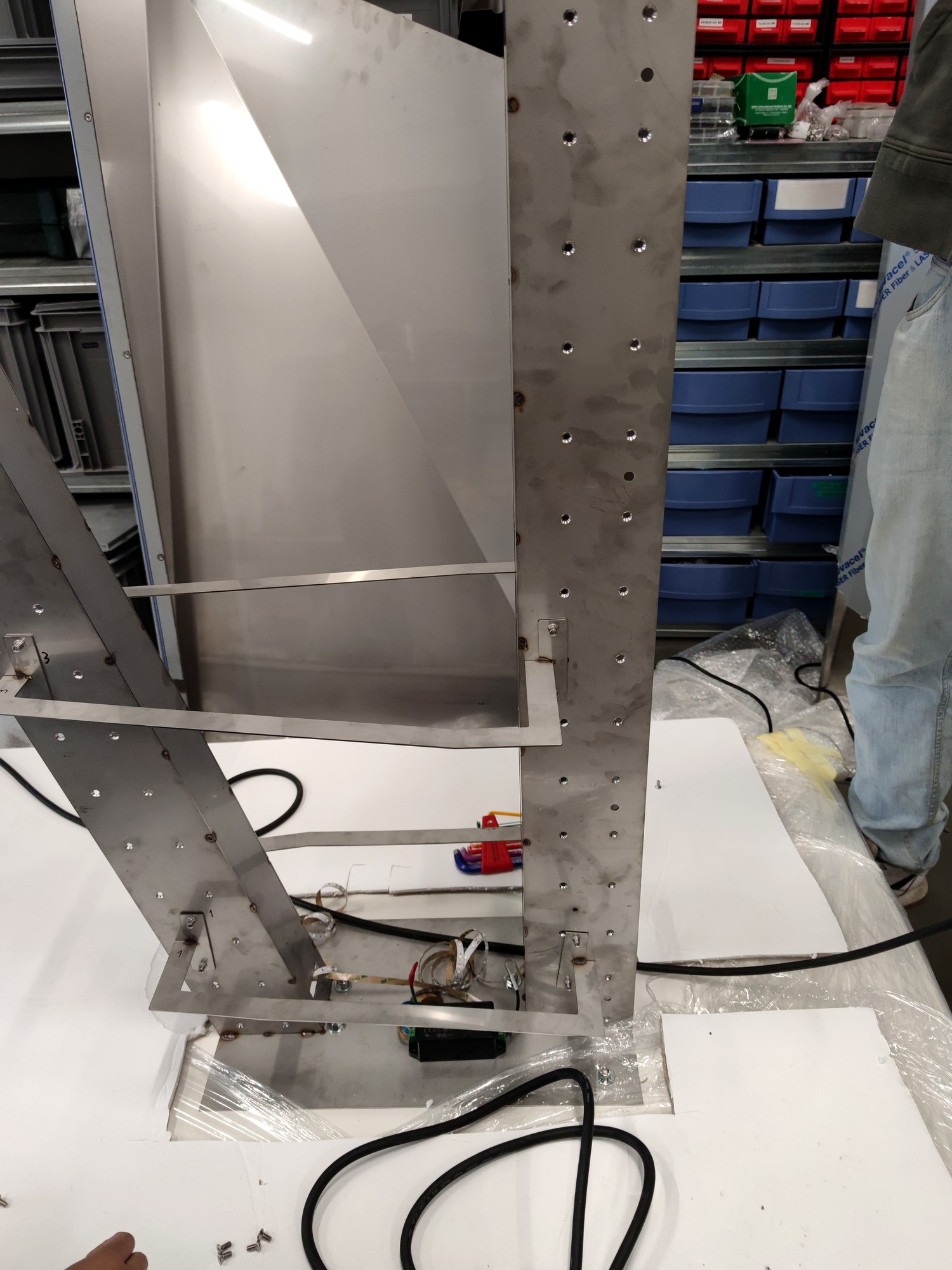 Perforated stainless steel pillar frame with wiring at the base on a white table