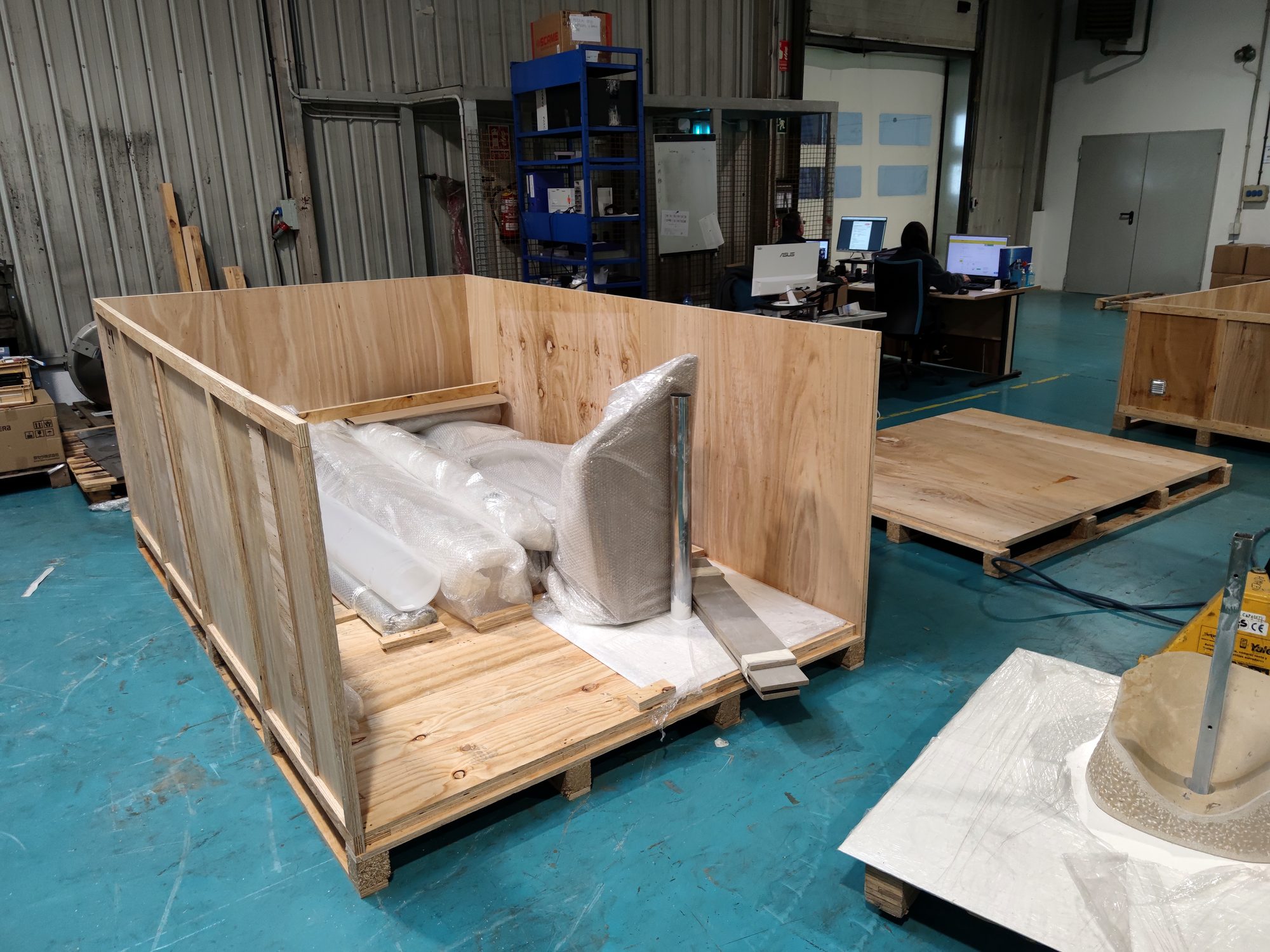 Open plywood shipping crate with stone-like parts and steel poles in a warehouse