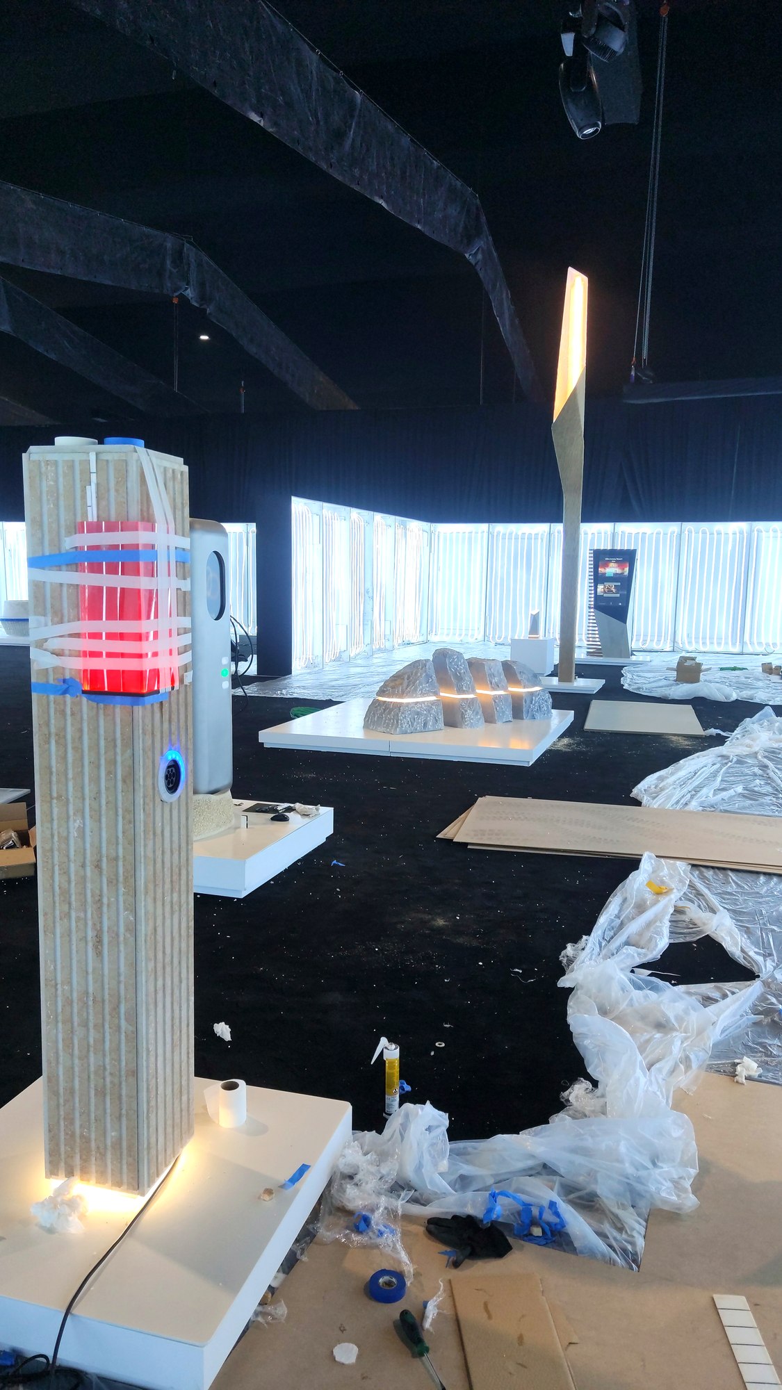 Event hall with ribbed pillar, glowing segmented stone benches, tall light pole, and installation materials