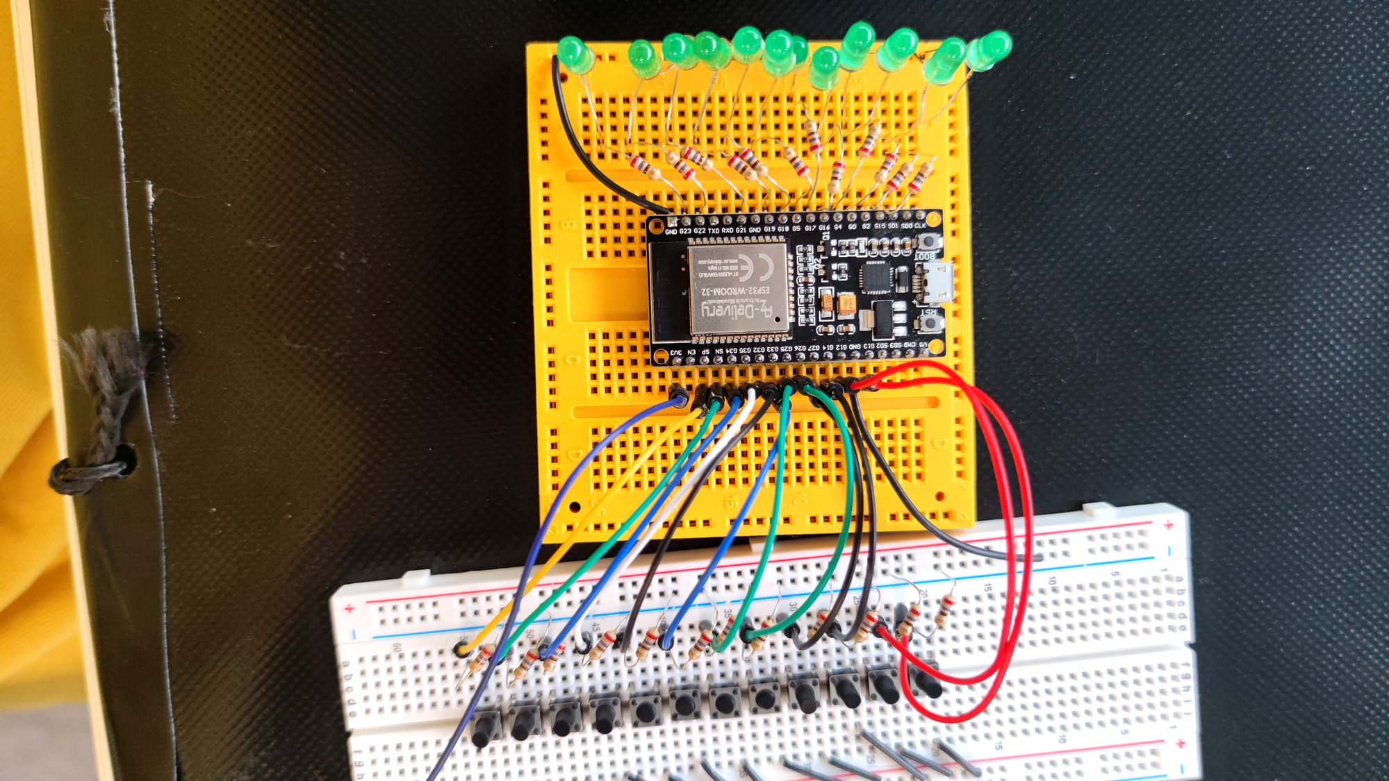 Yellow and white breadboards with an ESP32 module, green LEDs, and push-buttons