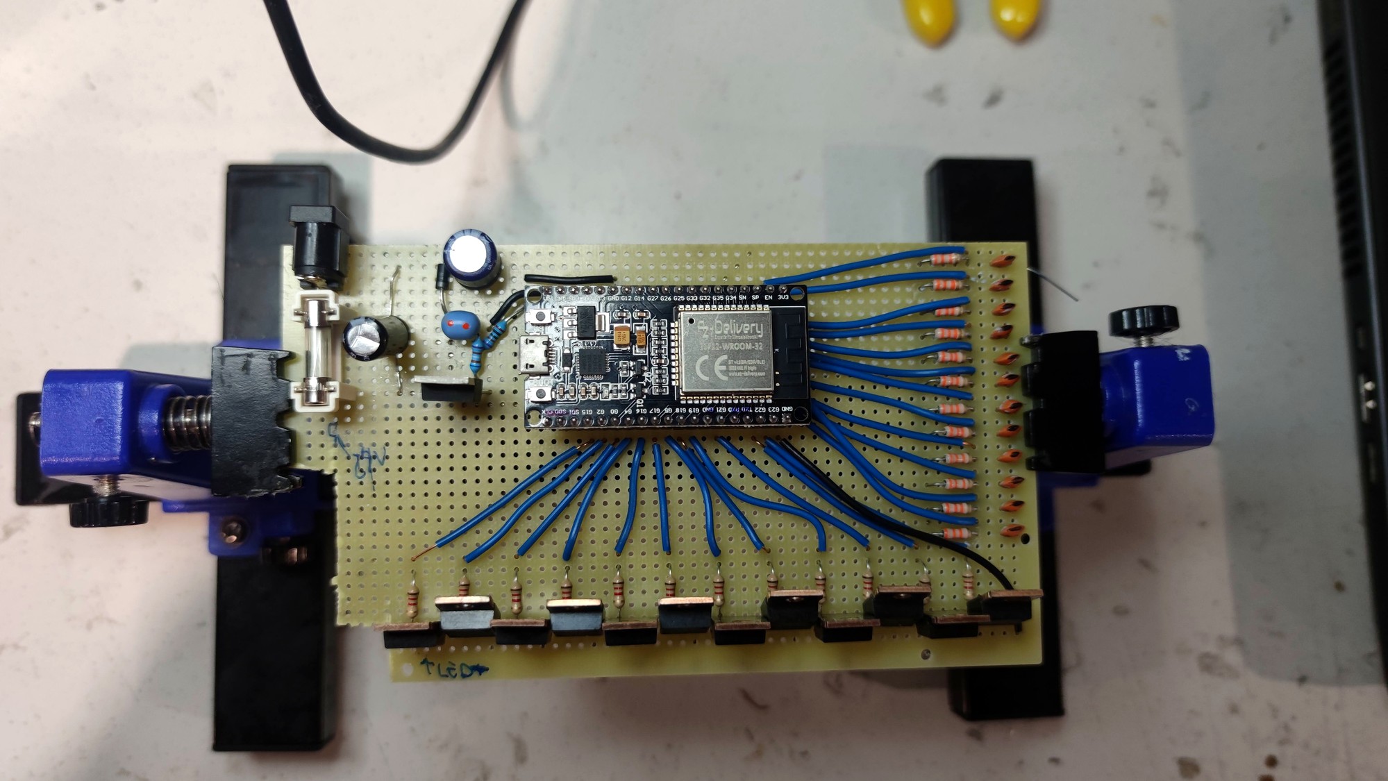 Perfboard with ESP32 and point-to-point wiring clamped in a blue PCB vise