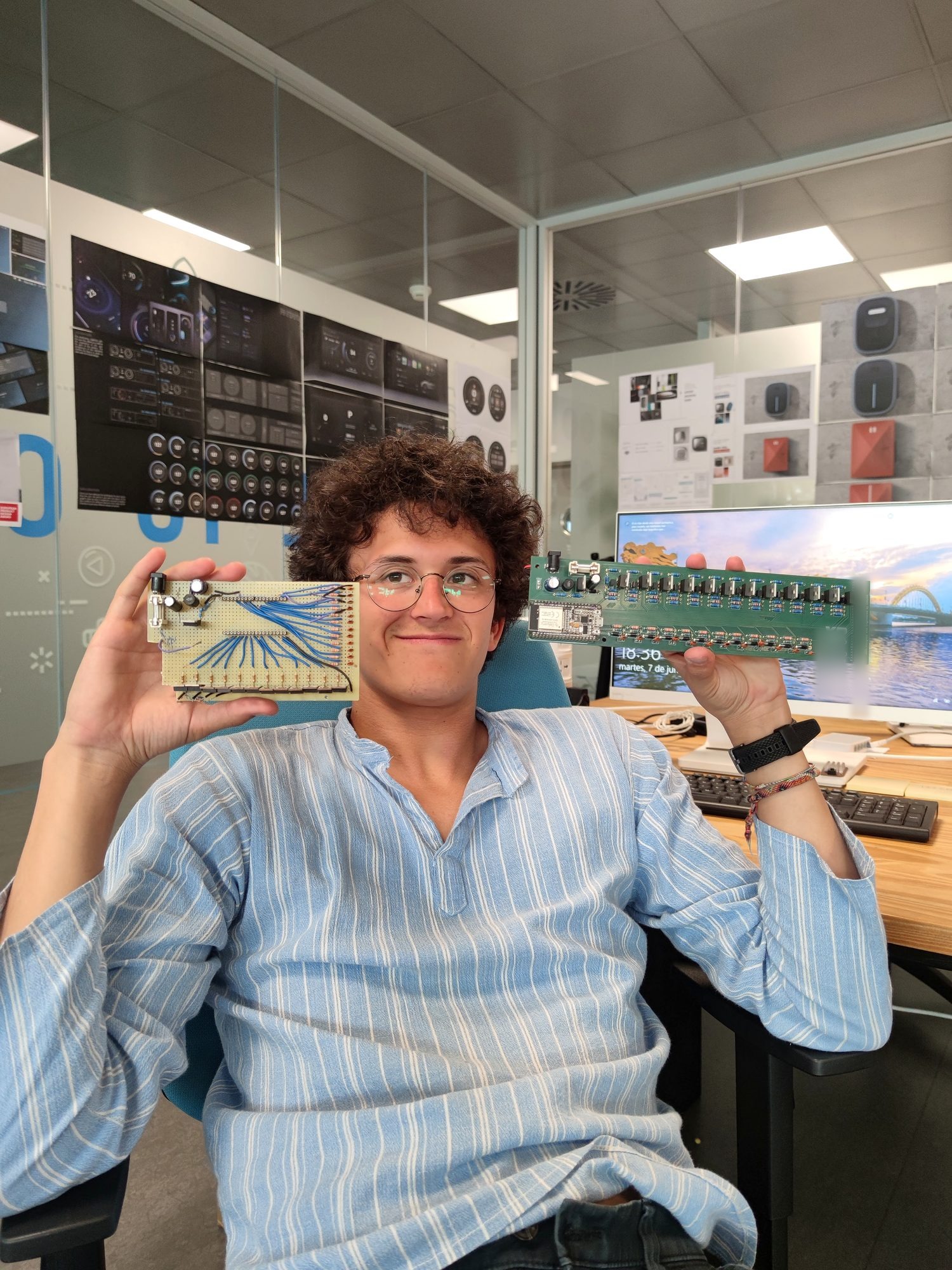 Person holding a wired perfboard prototype in one hand and a green custom PCB in the other