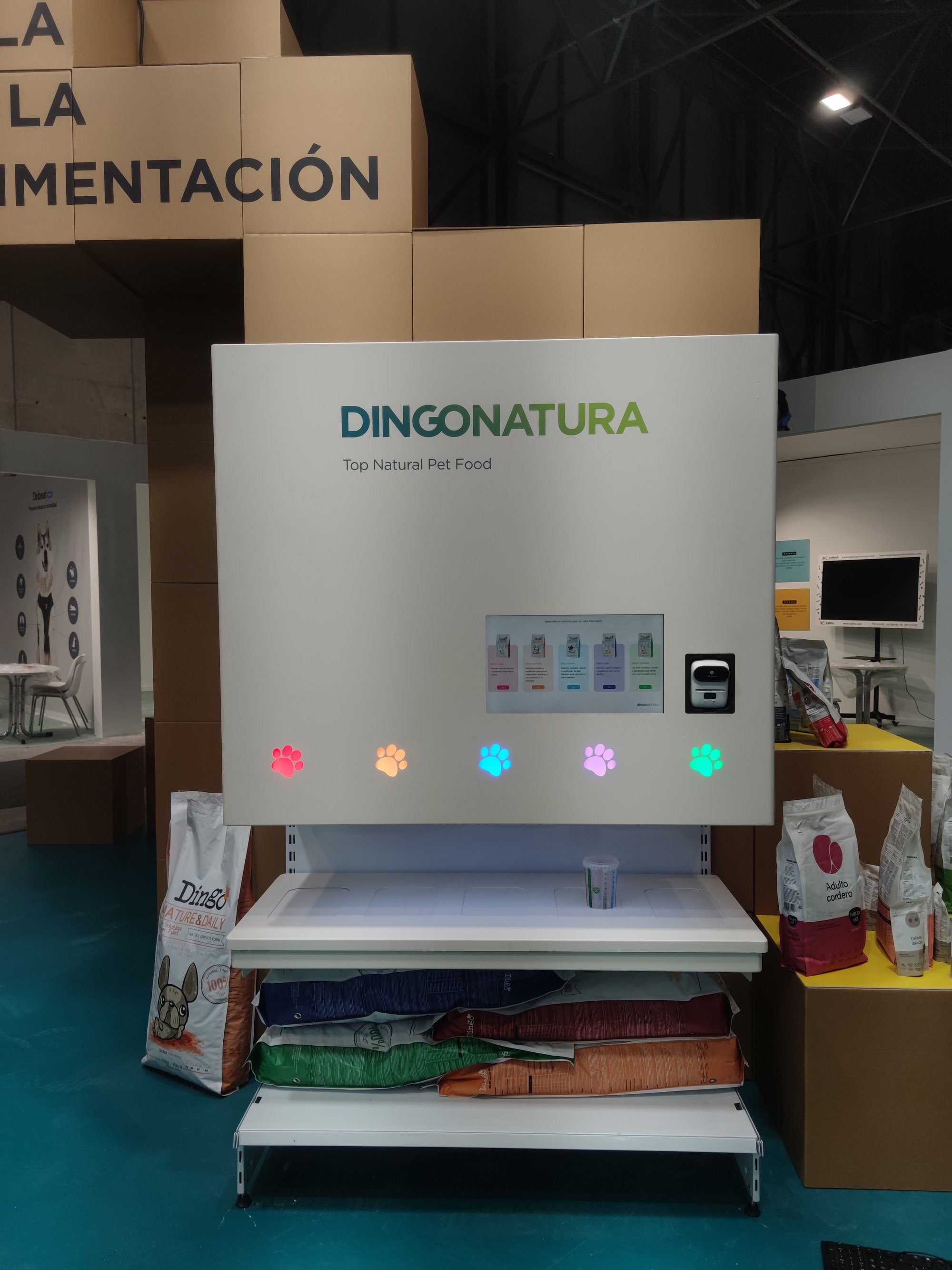 White Dingonatura smart pet-food dispenser booth with colorful paw-print buttons and product bags
